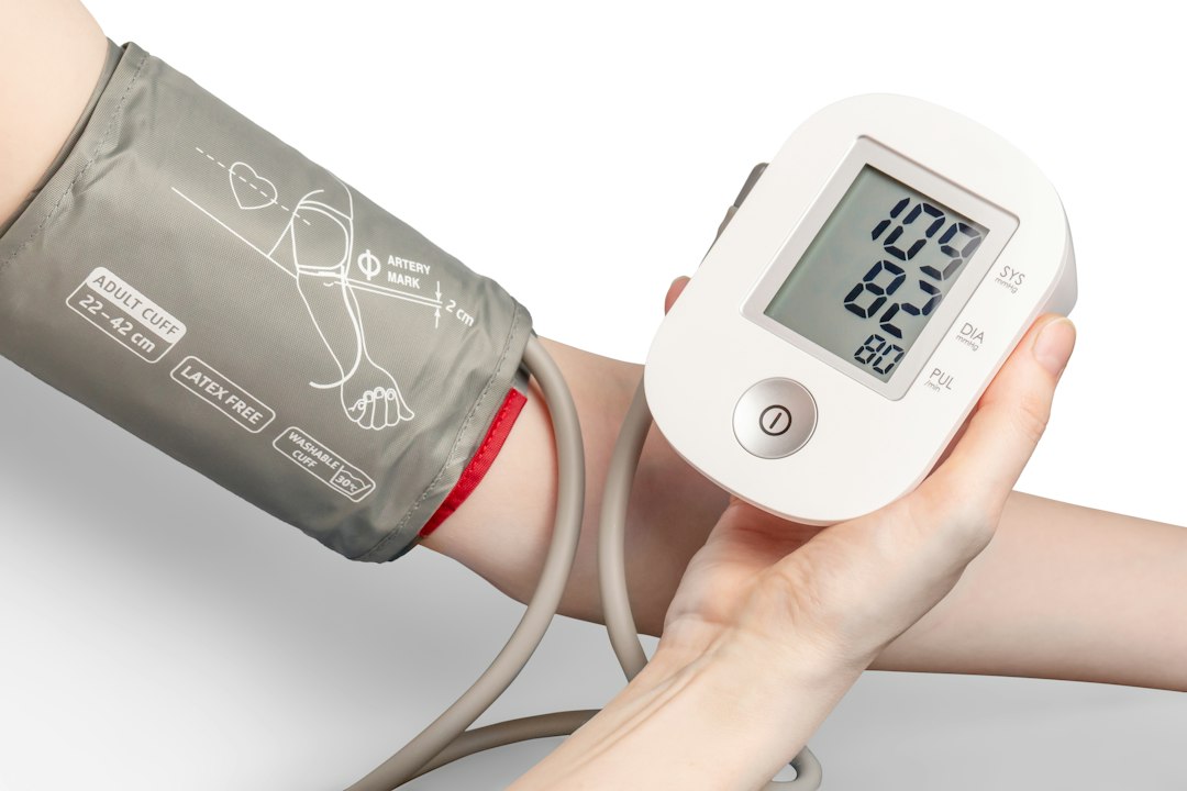 Hands using a digital blood pressure monitor on a white table